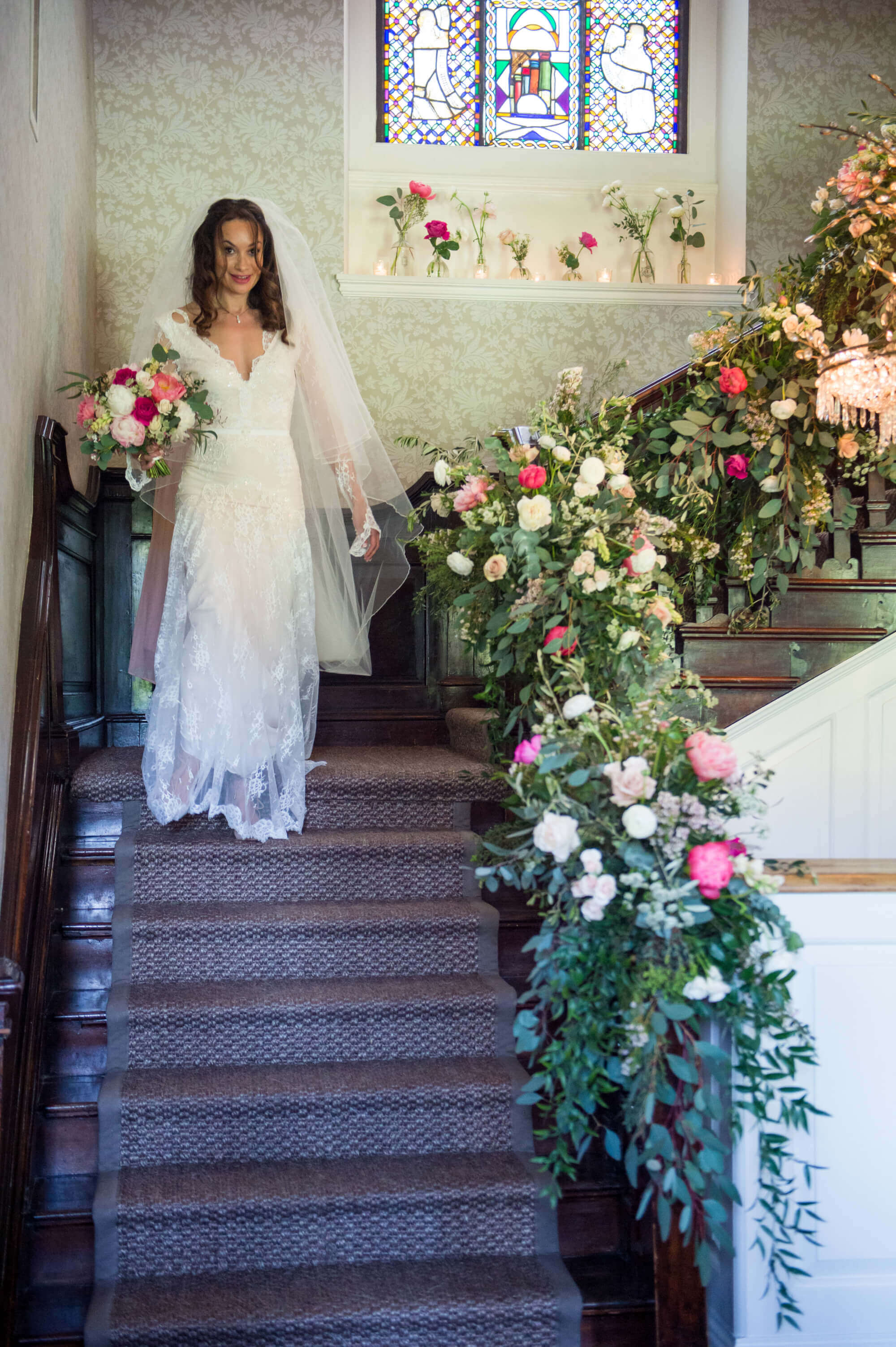 bride walking down the stairs at babington house with the bannister decorated with flowers