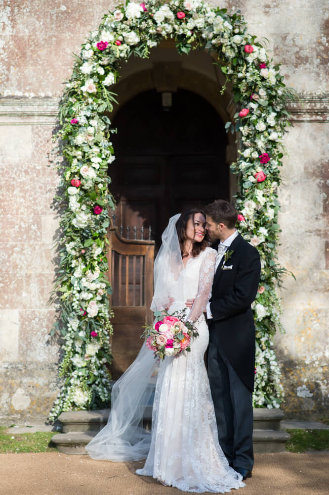 bride and groom next to babington house chapel with flower arch