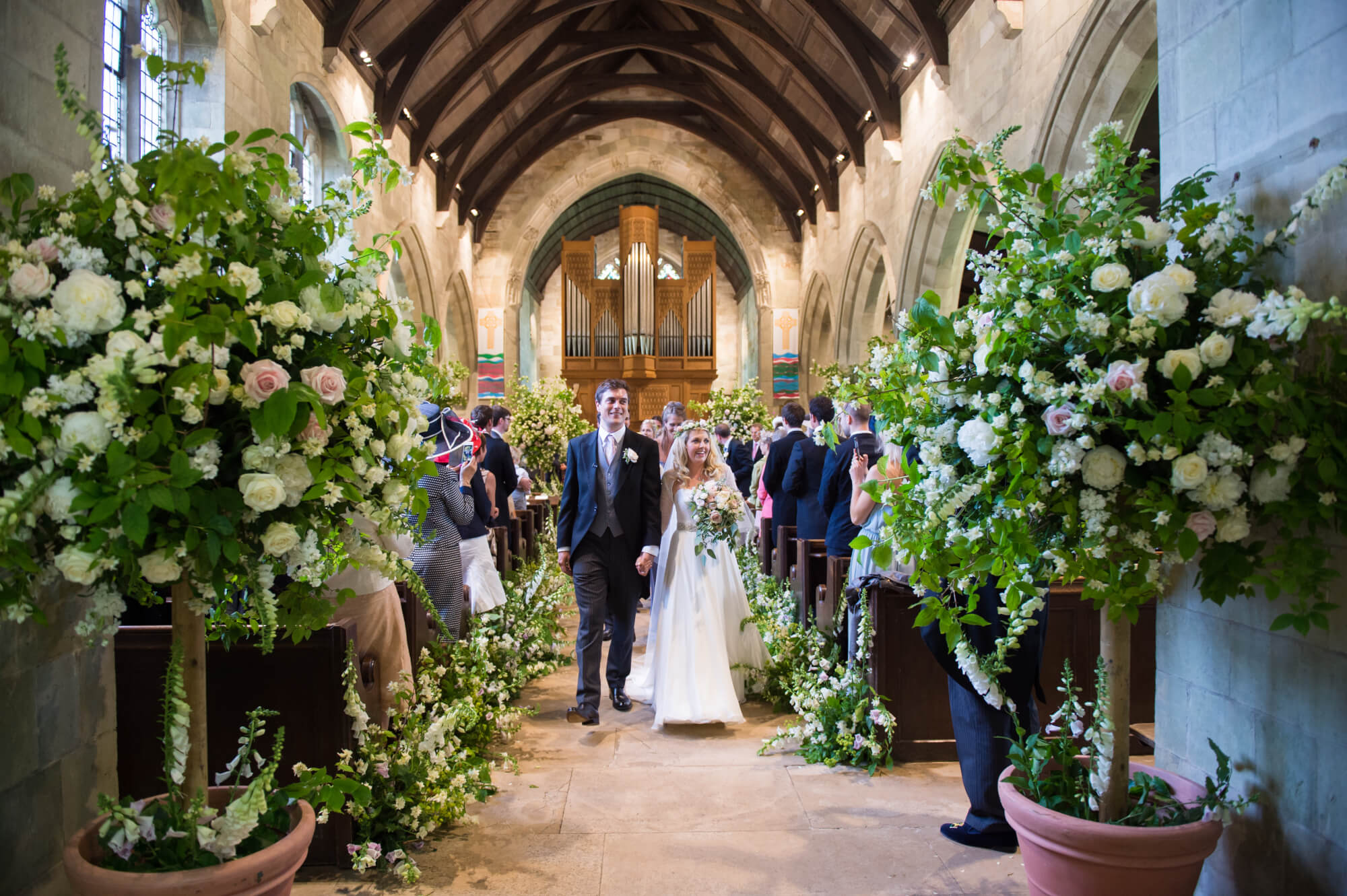 bride and groom leaving church with flowers and trees decorating the aisle at bryanston chapel