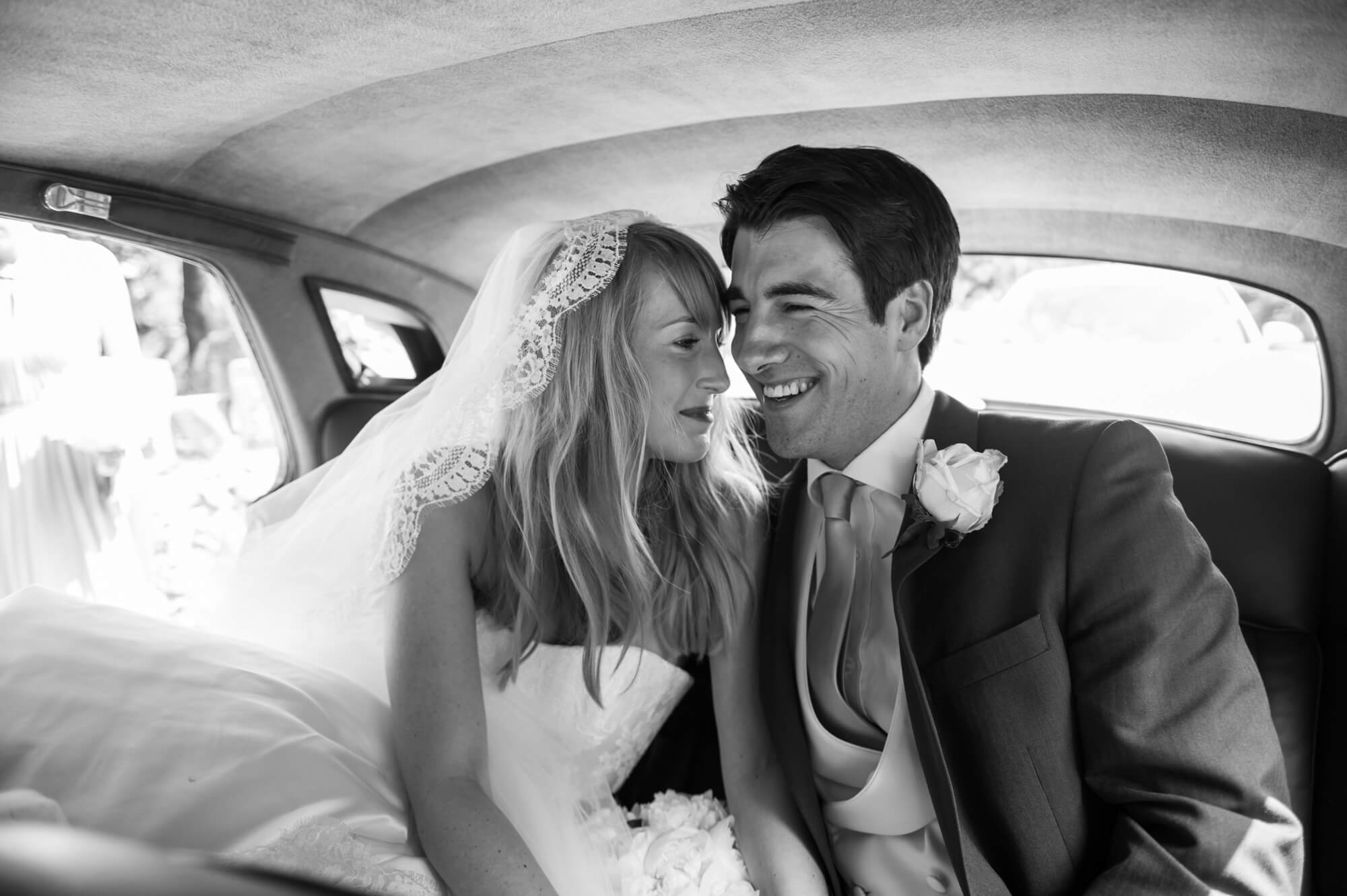 A bride and groom sitting next to each other in a vintage car
