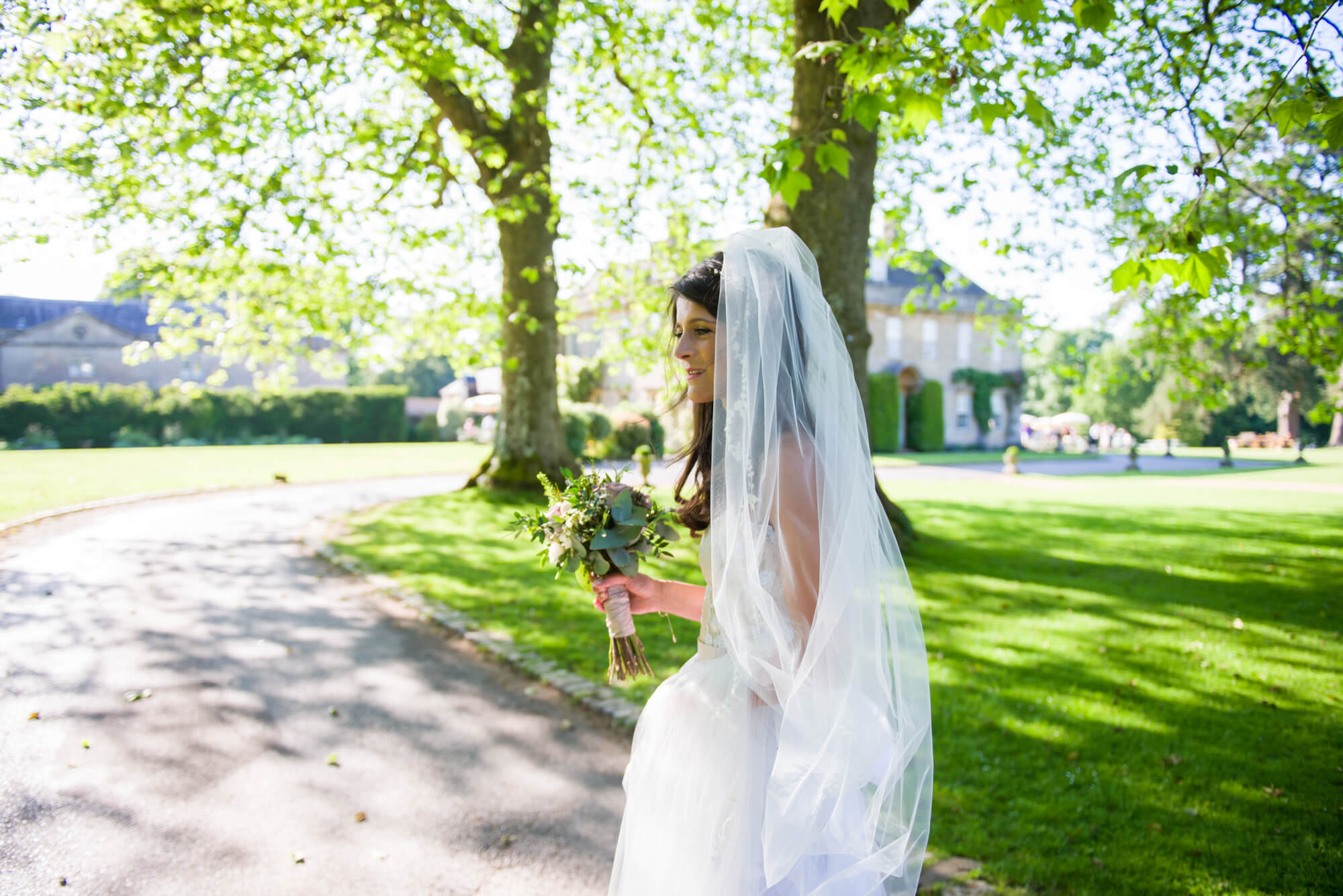 bride holding her bouquet and veil on babington house driveway