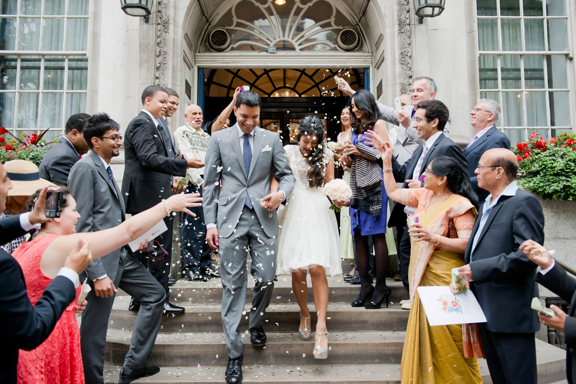 A bride and groom walking down the steps at Chelsea Town Hall having confetti thrown on them 