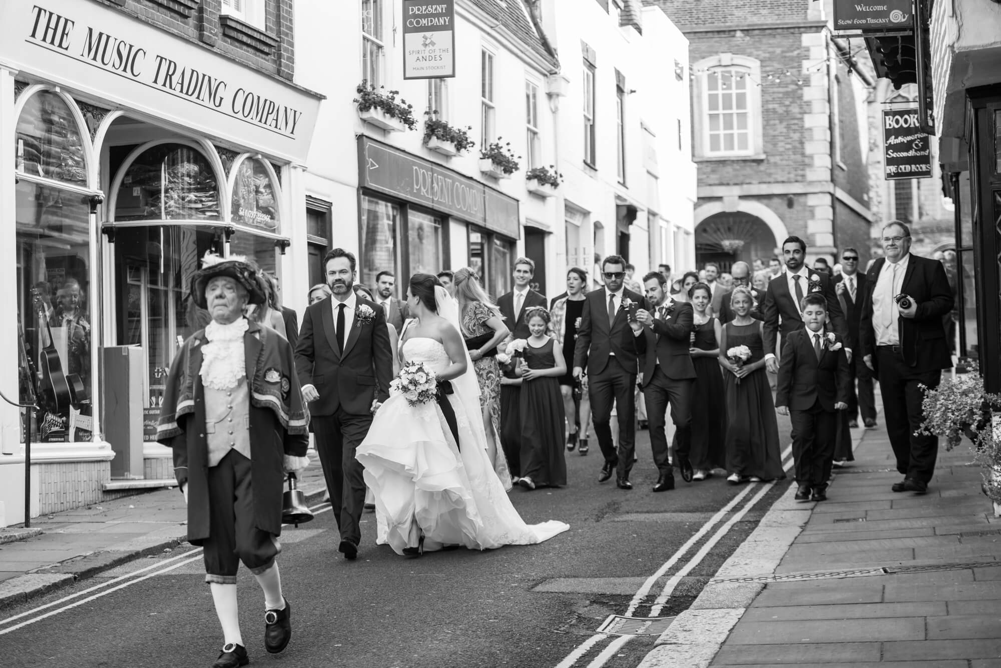 A bride and groom with their wedding party walking through the streets of Rye in East Sussex