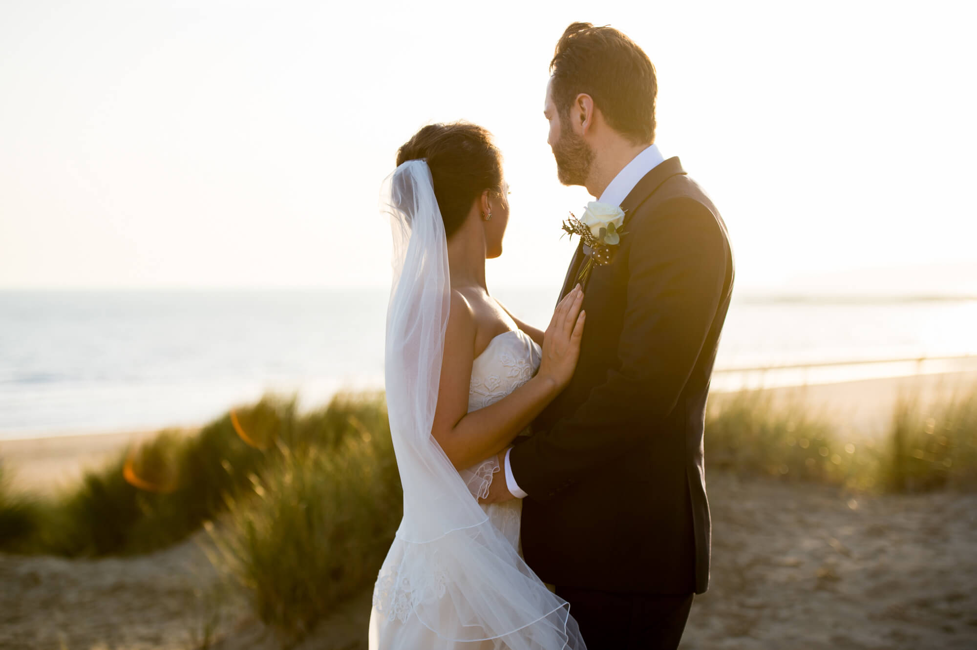A bride and groom on the beach at Camber sands looking into the sea as the sun sets