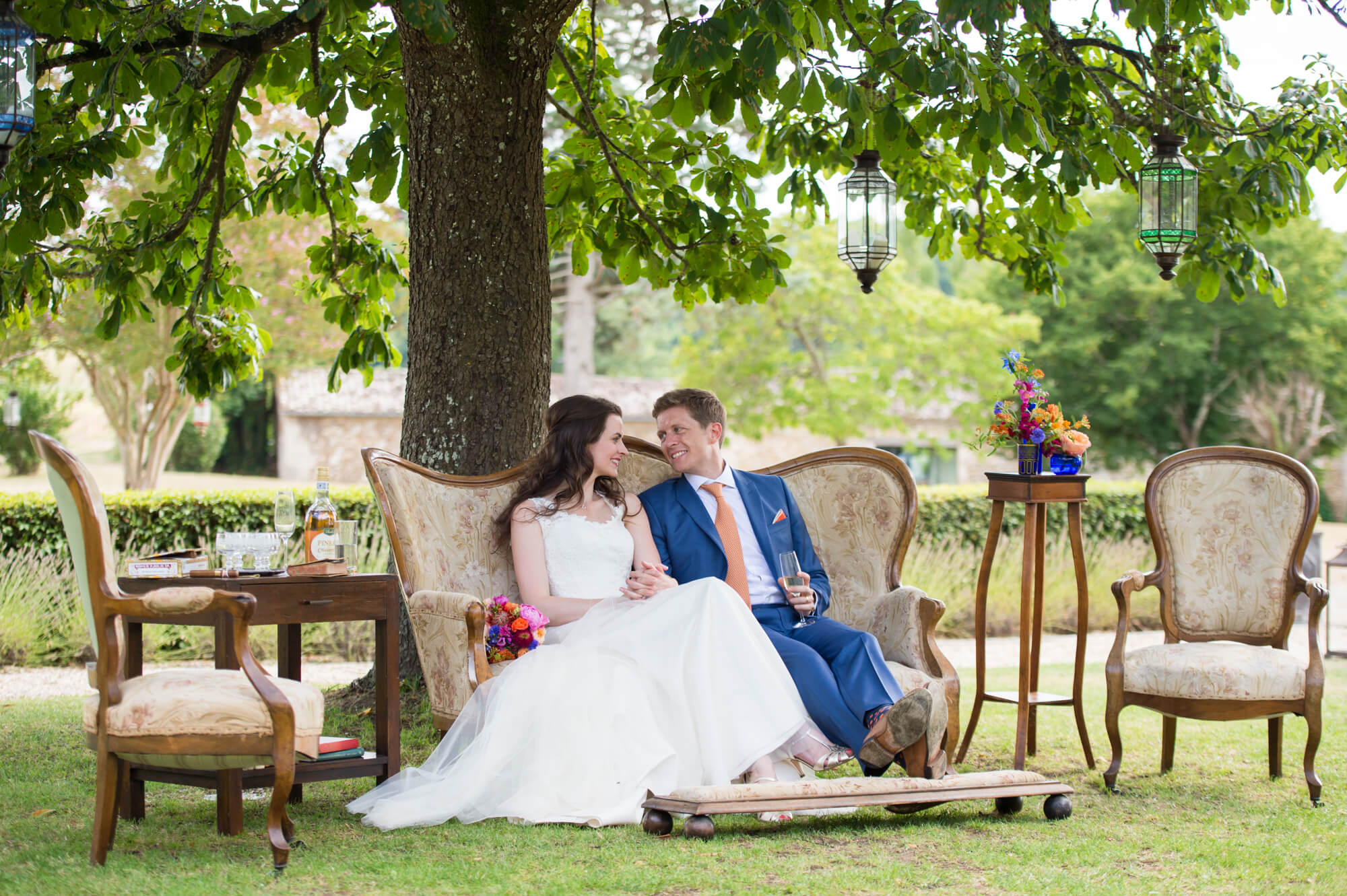 bride and groom sitting on vintage furniture under a tree at chateau rigaud