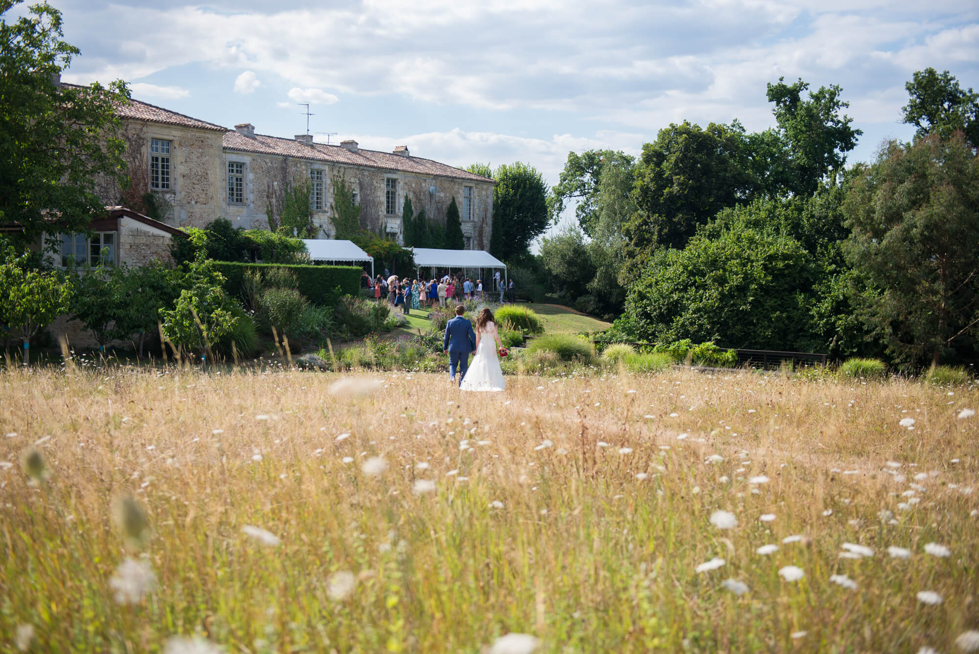 bride and groom walking through the flowers and long grass in the meadow at chateau rigaud