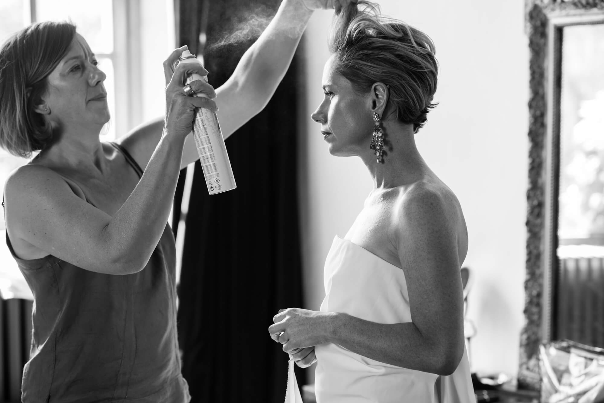 A black and white photograph of a bride having hairspray sprayed on her hair