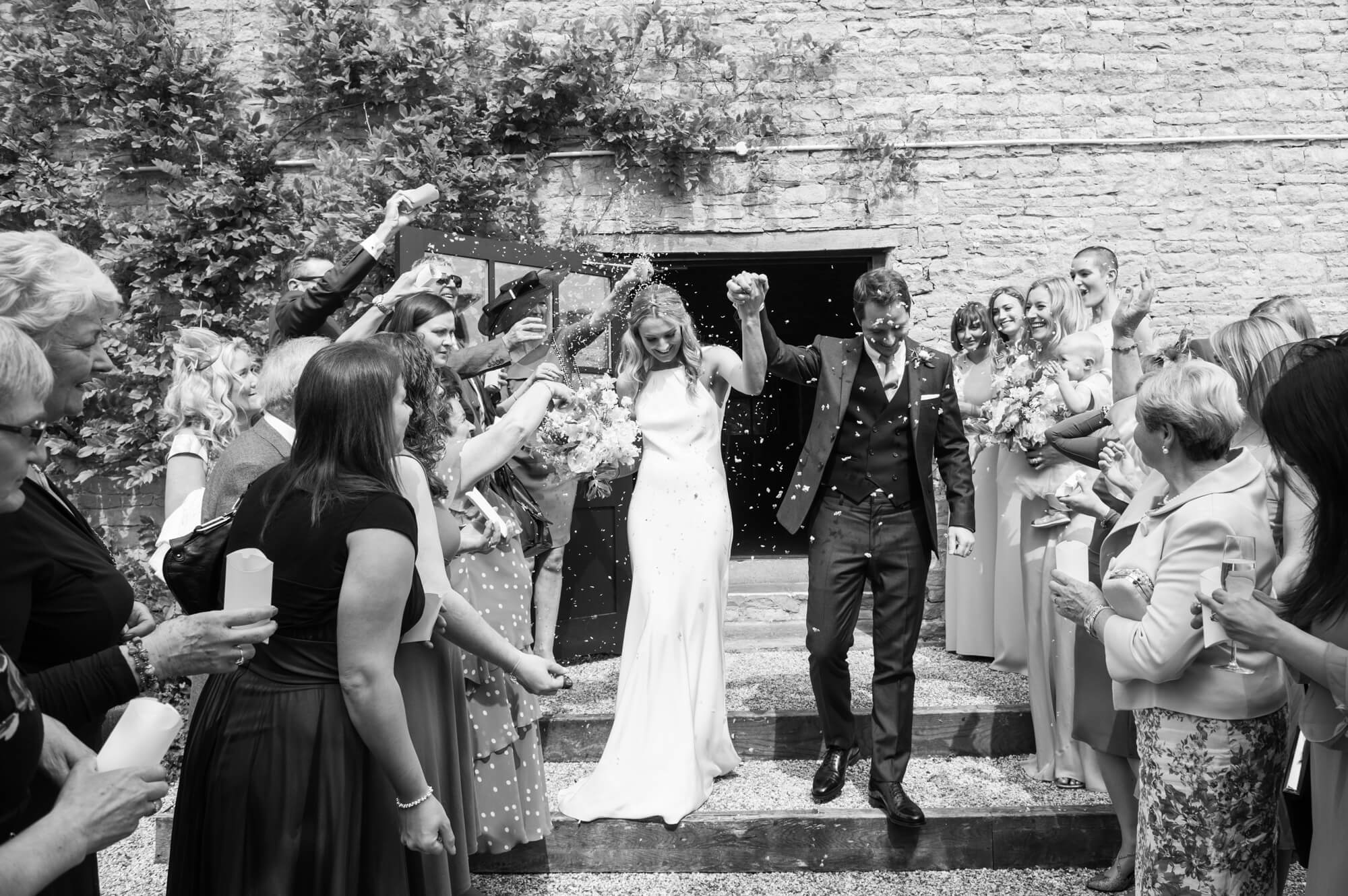 A newly married couple leaving Merriscourt barn with their hands in the air 