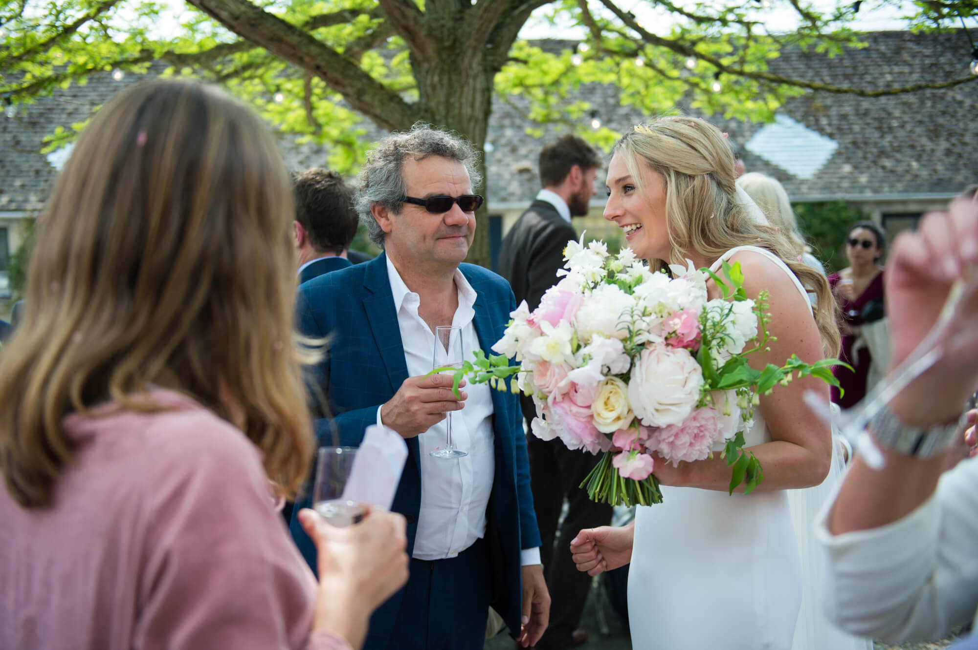 A bride holding her Rowan Blossom wedding bouquet whilst chatting to guests