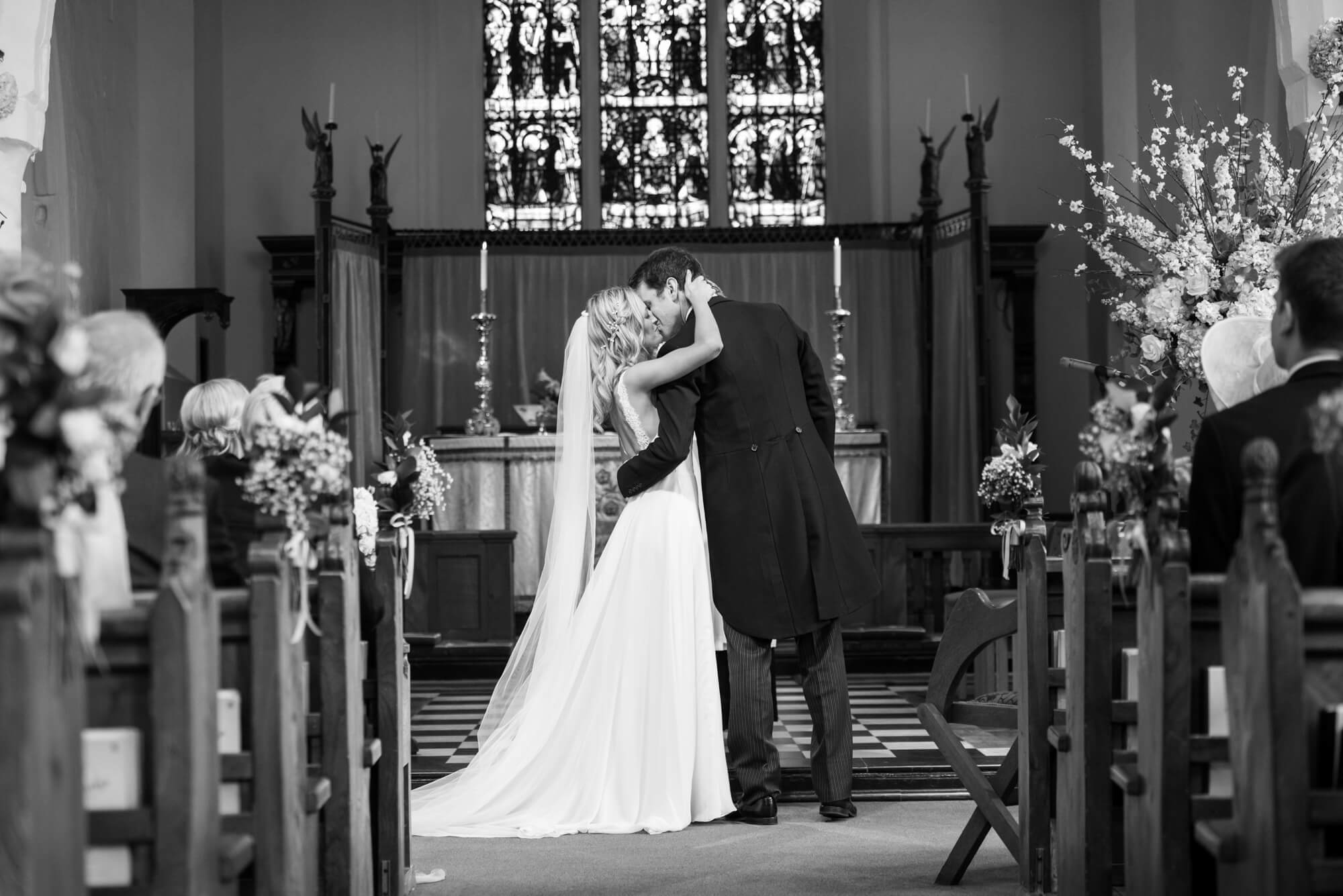 A black and white photo of a bride and groom kissing at the altar