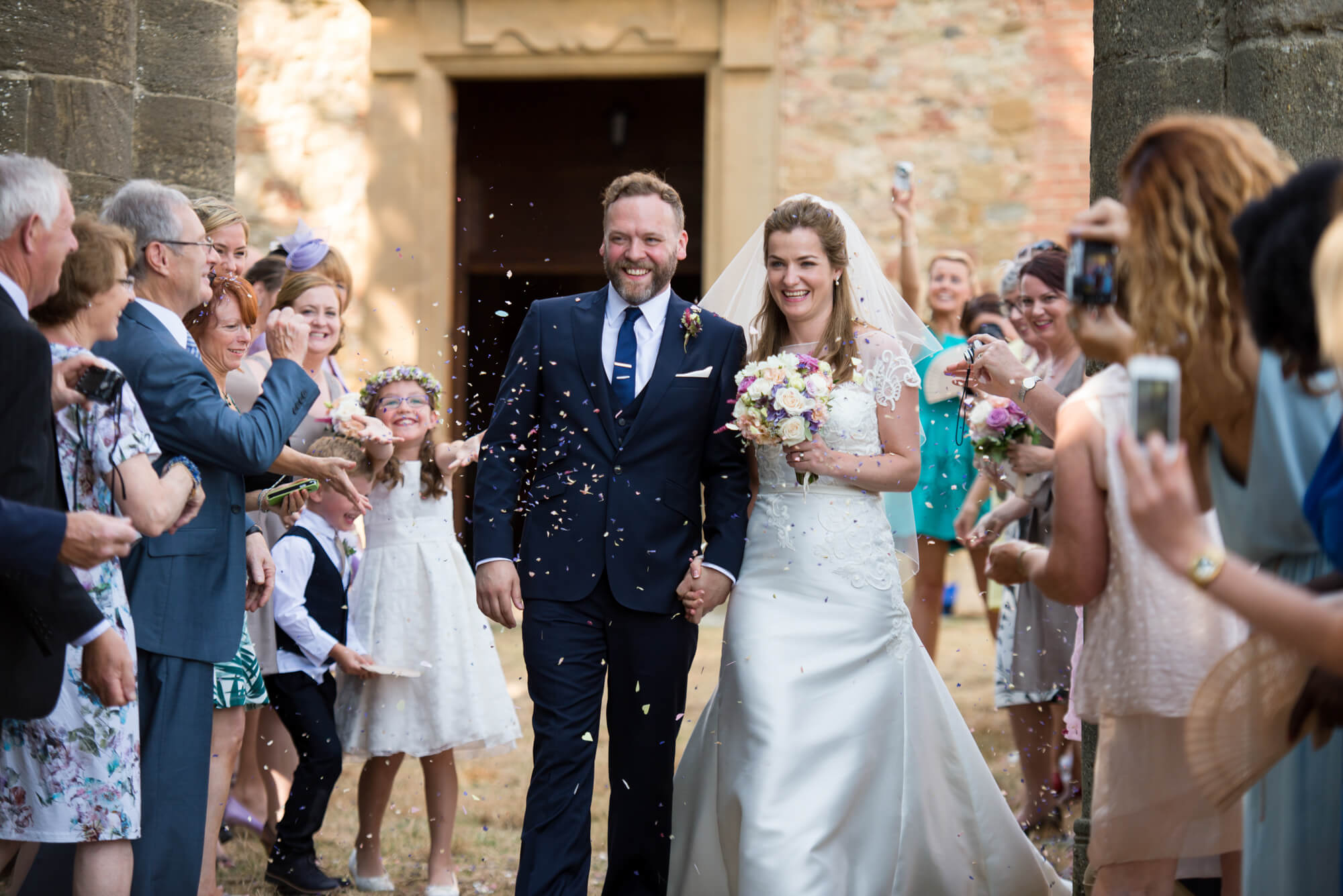 bride and groom leaving the church with confetti in tuscany destination wedding photographer