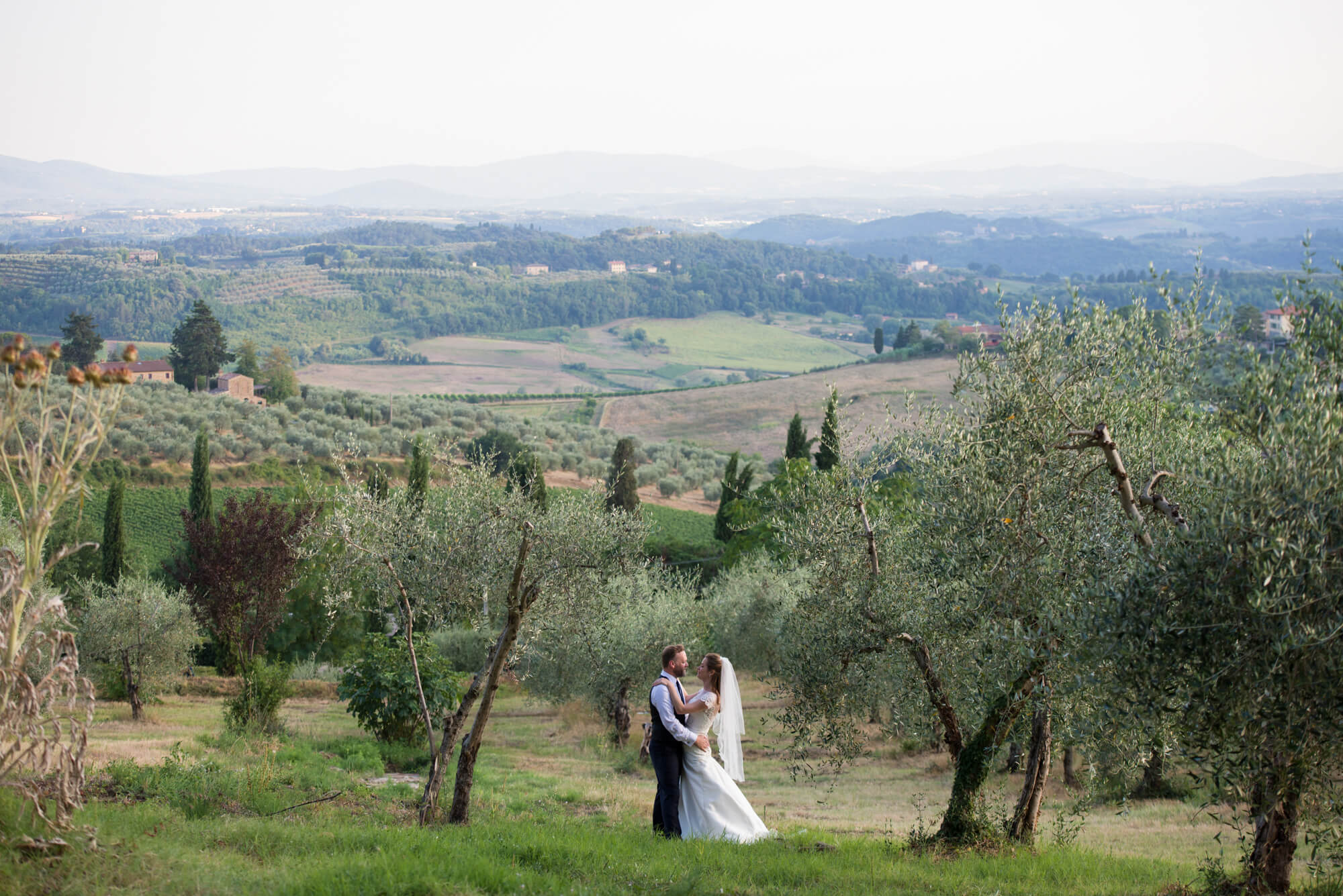 Bride and groom in olive grove with rolling tuscan hills in Italy 